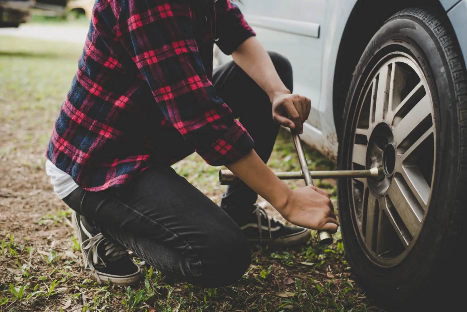 Woman inspecting a flat tyre on her car roadside — Alpha Brothers flat tire change service Sacramento
