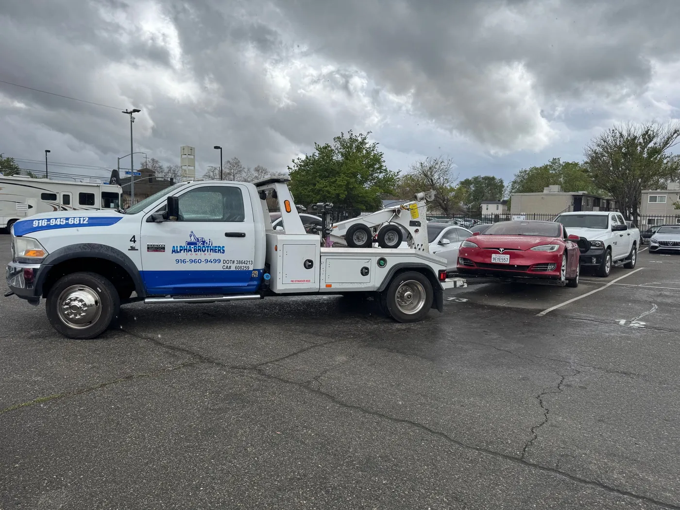 Alpha Brothers white Ram flatbed tow truck loading a red Tesla Model S electric vehicle in a Sacramento parking lot