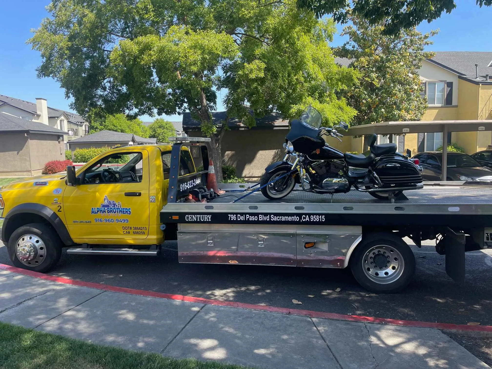 Alpha Brothers yellow Ram flatbed tow truck transporting a Harley-Davidson motorcycle in a Sacramento neighborhood